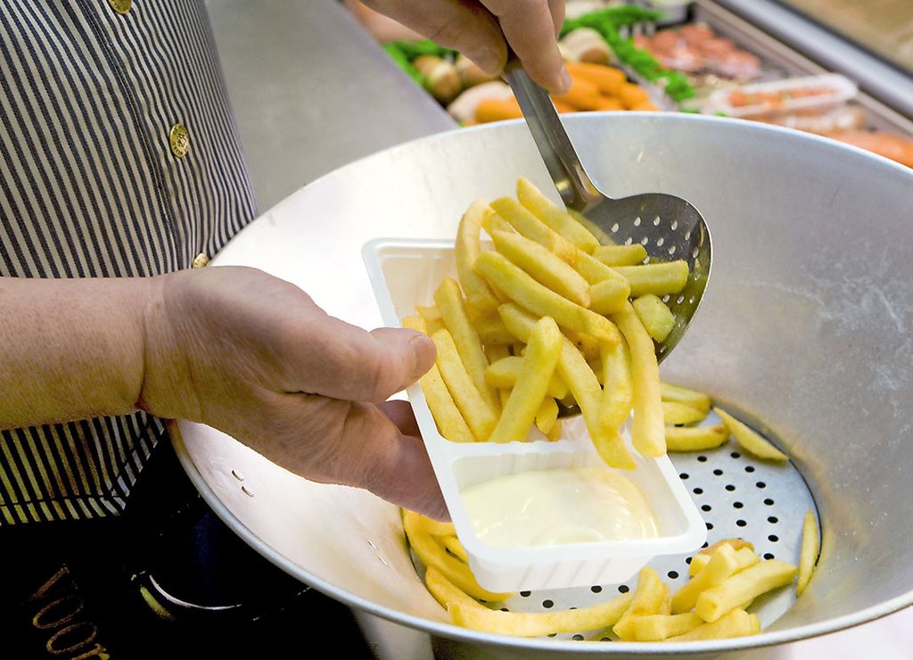 Frites wordt in een plastic bakje geschept. Voor afhalen en bezorgen moeten ondernemers per 1 juli 2023 een meerprijs in rekening brengen bij de consument voor eenmalige verpakkingen en drinkbekers die plastic bevatten. Foto: ANP