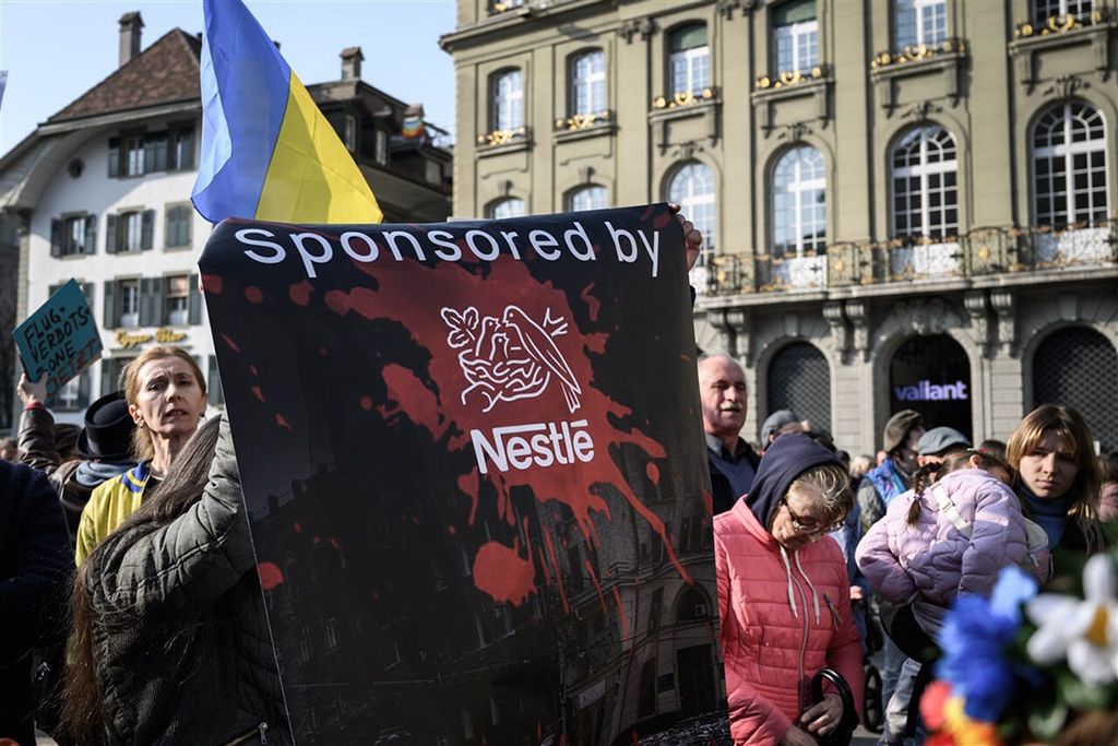 Demonstranten houden een spandoek vast tegen de Zwitserse voedselgigant Nestlé tijdens een demonstratie tegen de Russische invasie van Oekraïne naast het Zwitserse parlementsgebouw in Bern. Foto: ANP
