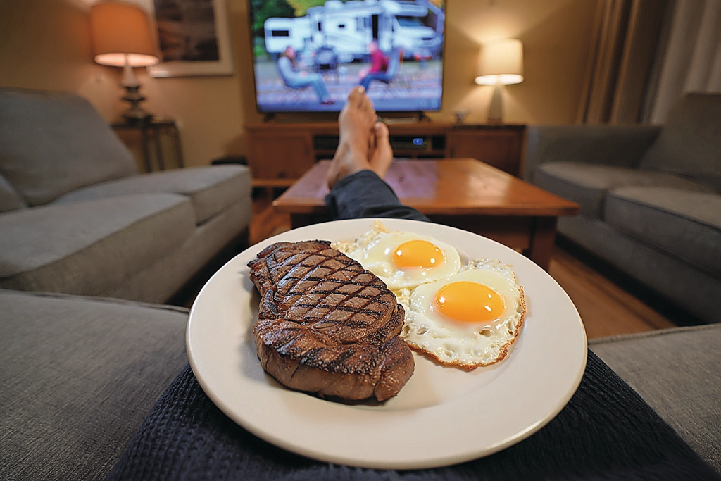 Met een bord met vlees en eieren op schoot voor de tv. Foto: Deze afbeelding is met behulp van AI gemaakt (Reve.art)